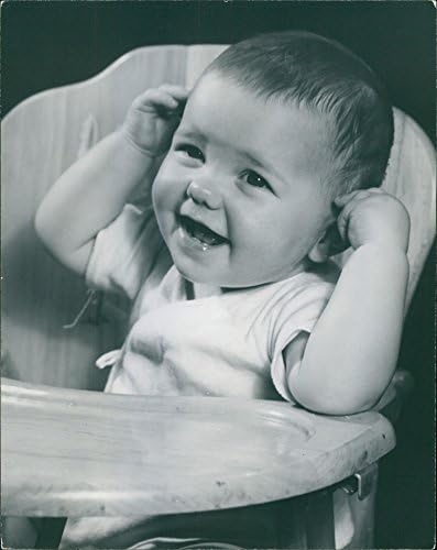 תצלום וינטג 'של תינוק יושב על כסא גבוה, מחייך.